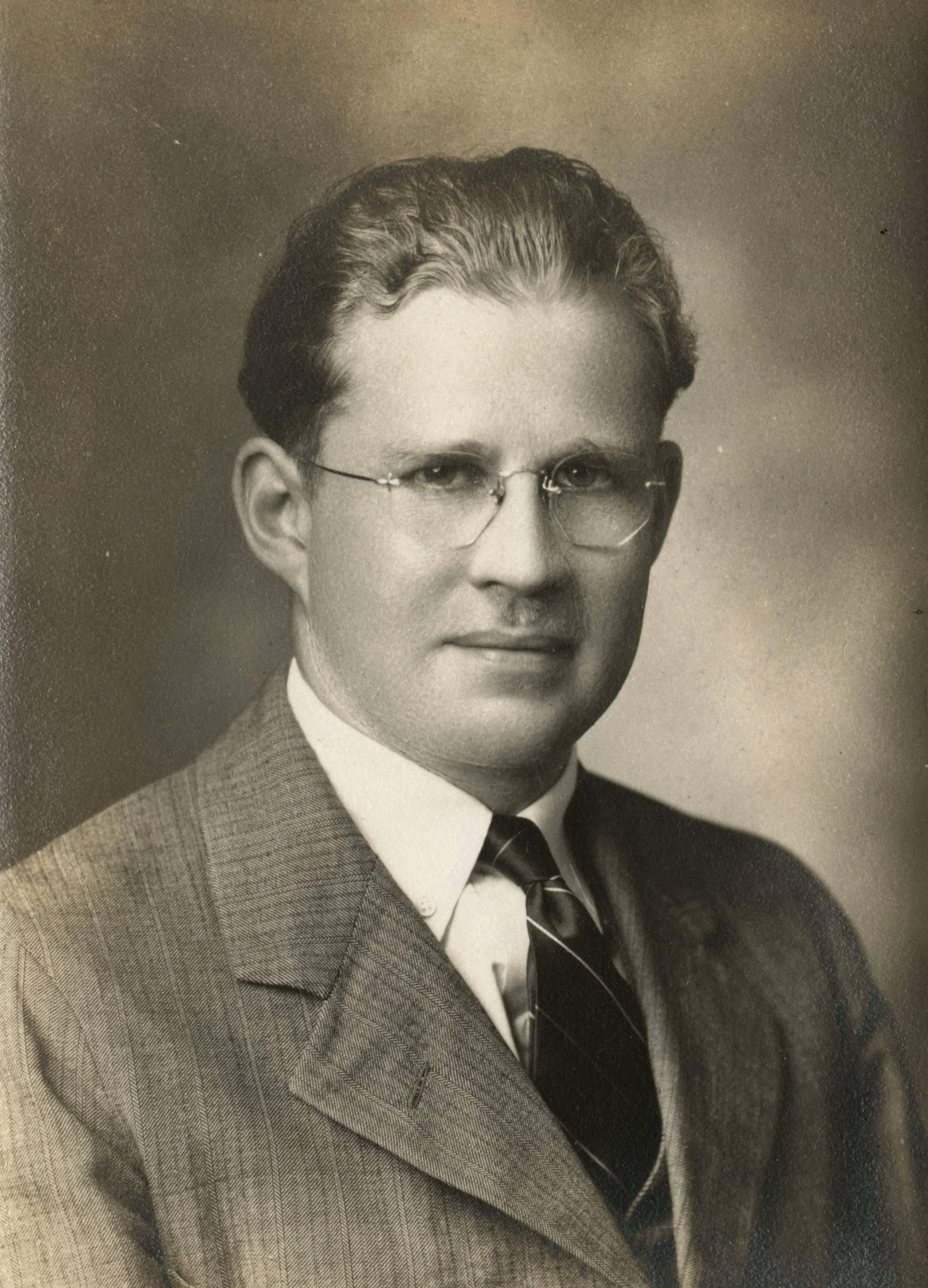 A young Wilfrid Sellars gazes forward. The picture is an old black and white and he is in his 20's or 30's wearing a tweed jacket.